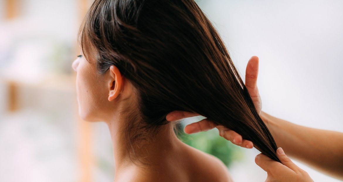Mulher branca de costas fazendo nutrição capilar no cabelo liso